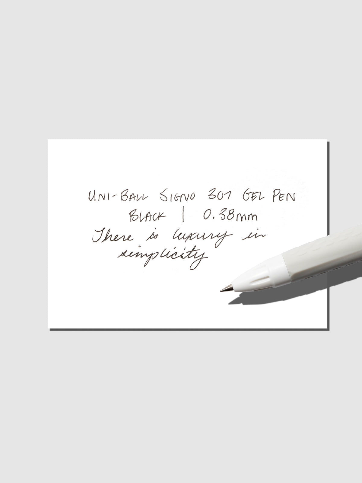 Uni-Ball Signo Gel pen resting on a pen test sheet. The sheet shows the pens specs. Color pictured is Black.