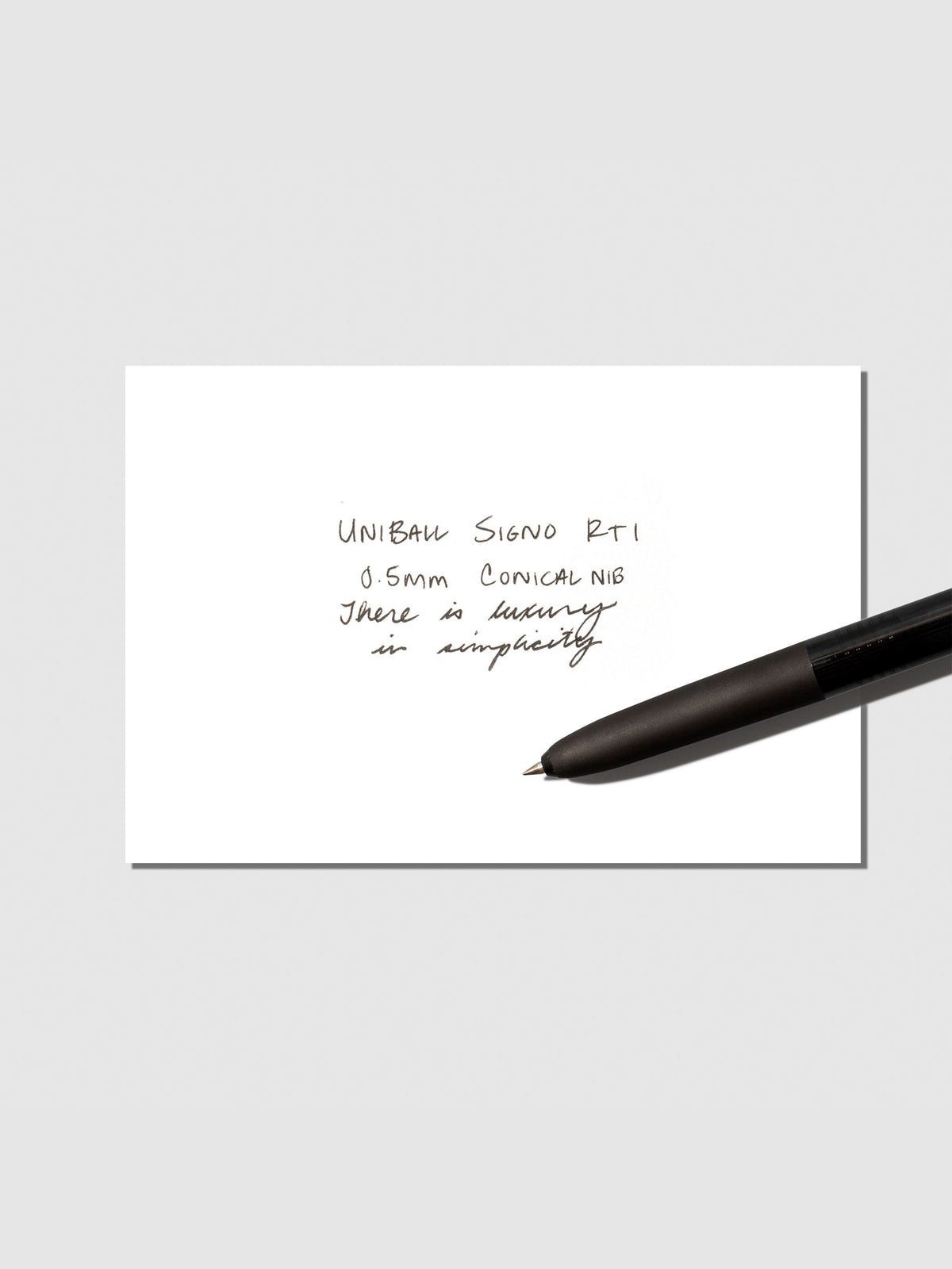 Uni Ball Signo in Black displayed with writing sample on a neutral background.