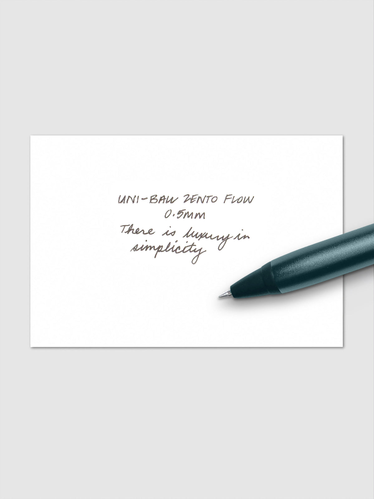 Handwritten writing sample using the Uni-ball Zento Flow Pen in a 0.5 mm nib. Shown with dark green-blue pen resting across paper.