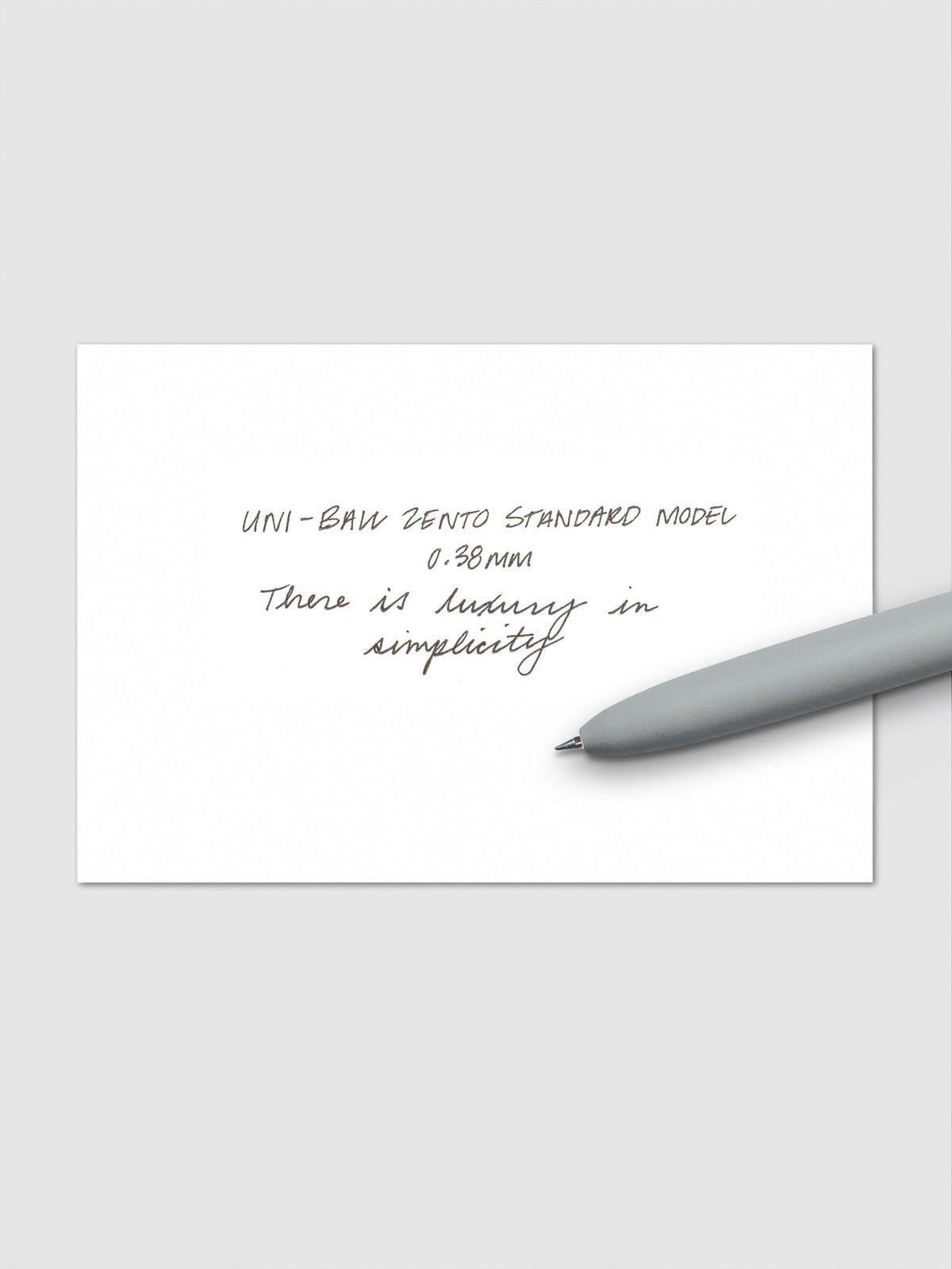 Handwritten sample using the Uni-ball Zento Standard Model Pen with black ink and a 0.38 mm nib. Shown with grey pen resting across paper.