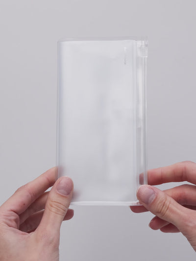 Pocket Plus travel notebook storage holder in clear frosted plastic being opened to show two zippered pouches with stickers and cards inside
